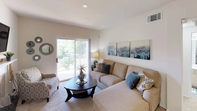 Modern living room with sectional sofa, armchair, coffee table, and balcony access.