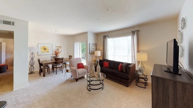 Living room and dining area in a furnished apartment with a sofa, chairs, dining table, and TV.