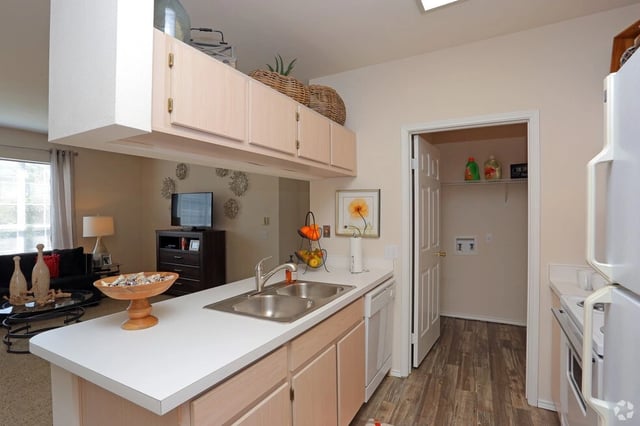 Kitchen with a double sink and dishwasher, overlooking a living area with a TV.