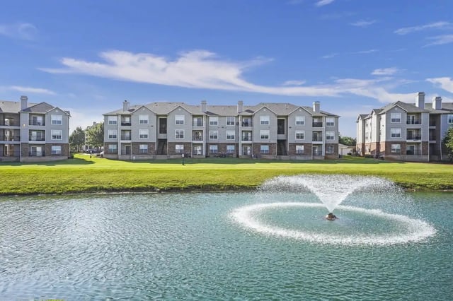 Exterior view of a multi-building apartment complex with a central pond and fountain.