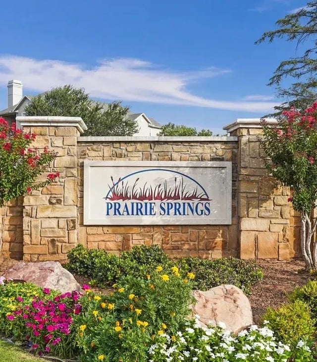 Stone entry sign at Prairie Springs with a landscaped bed and colorful flowers.
