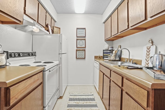 Kitchen with wooden cabinets, white appliances including stove and refrigerator, and a sink.