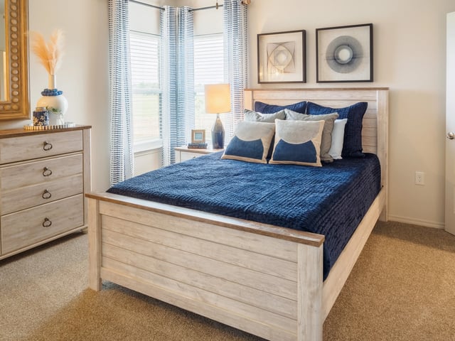 Bedroom with light wood bed frame, navy blue quilt, matching pillows, and striped curtains by the window.