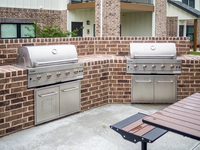 Two stainless steel outdoor grills set into brick counters in a communal patio.