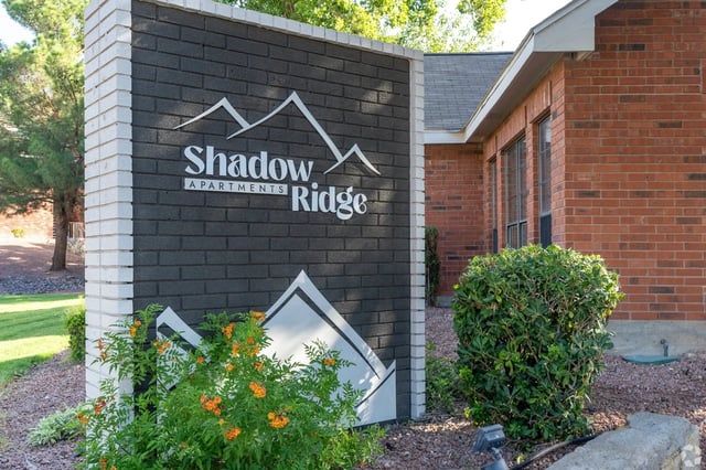 Exterior sign for Shadow Ridge Apartments mounted on a brick wall with landscaping.