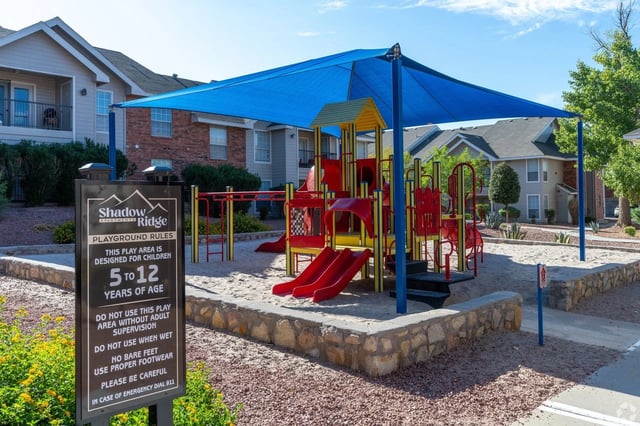 Community playground with red slides under a blue shade canopy at an apartment complex.