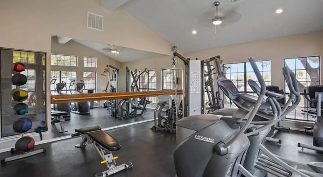 Indoor apartment gym with cardio machines, weights, and mirrors.