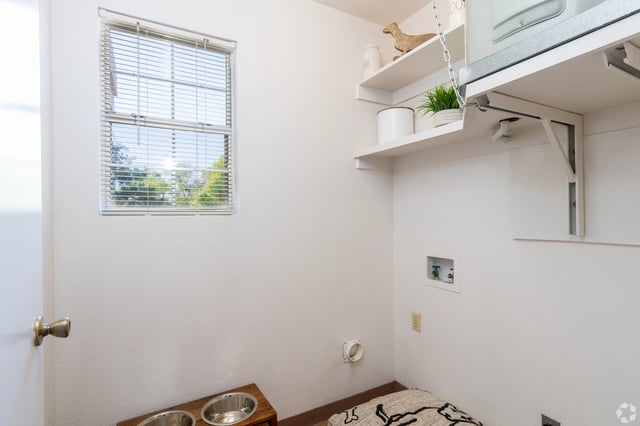 Interior view of a laundry area with a window, washing machine hookups, and pet bowls.