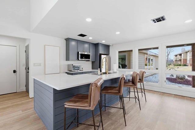 Bright modern kitchen with blue-gray cabinets, white counters, a central island, and large windows.