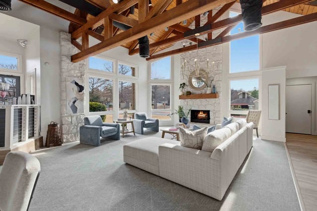 Bright living room with stone fireplace, large windows, and exposed wooden beams.