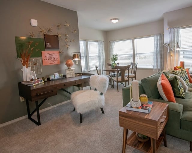 A home office setup with a wooden desk, white fluffy chairs, and wall decor.
