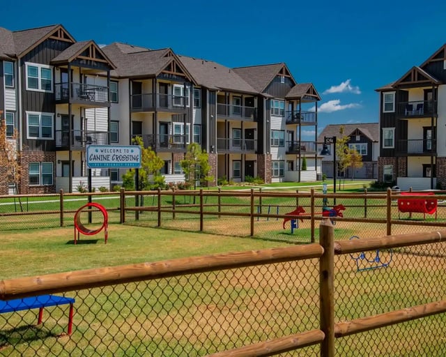 Exterior of a multi-building apartment community with a fenced dog park and playground.