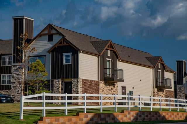 Exterior view of a modern multifamily building with stone accents, balconies, and a white fence.