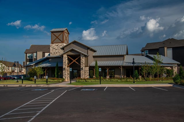 Exterior view of a multifamily community building with stone entrance, metal roof, and front parking lot.