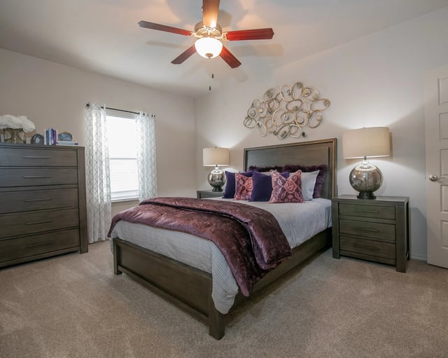 Bedroom with dark wood bed frame, two nightstands, dresser, ceiling fan, and wall art.