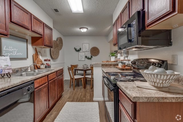 Kitchen with dark wood cabinets, stainless steel sink, dishwasher, and dining area.