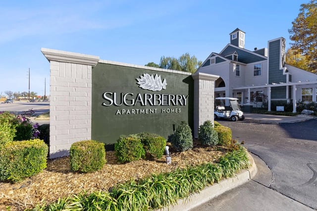 Exterior Sugarberry Apartment Homes sign with landscaping and building in background.