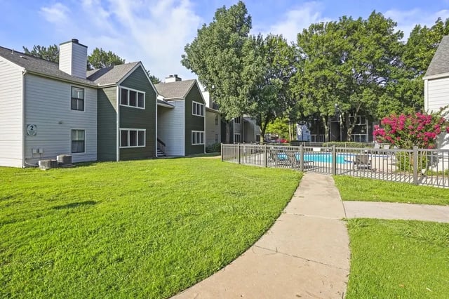 Exterior view of apartment buildings with a grassy lawn and a fenced pool area.