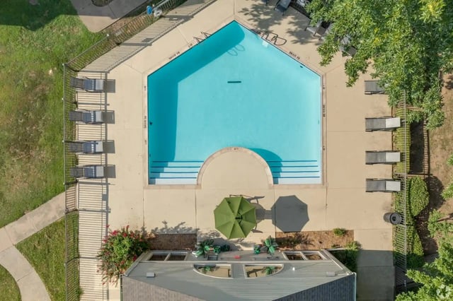 Aerial view of a blue pool surrounded by lounge chairs and umbrellas on a concrete deck.