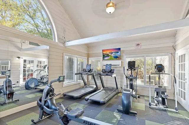 Bright on-site fitness center with treadmills, ellipticals, bikes, mirrors, and a TV.