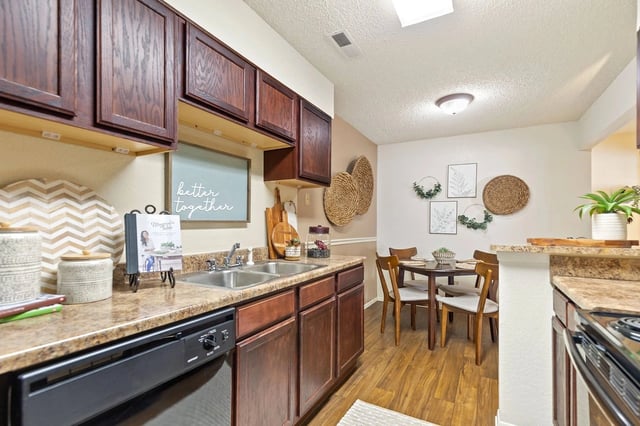 Kitchen with dark wood cabinets, granite counters, and a dining area in an apartment.