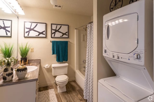 Modern bathroom with stacked washer and dryer, vanity, toilet, and shower.