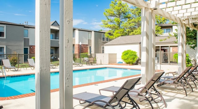 Outdoor apartment community pool with lounge chairs under a white pergola.