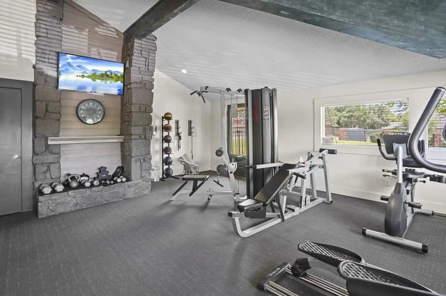 Indoor apartment community gym with weight rack, benches, and cardio machines.