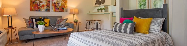 Furnished apartment interior with a bed, gray sofa, coffee table, and a kitchenette bar area.