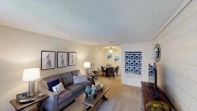 Living room with gray sofa, coffee table, dining area with table and chairs, and entertainment center.