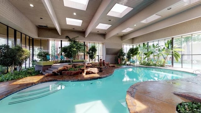 Indoor swimming pool with rock waterfall and lush greenery.