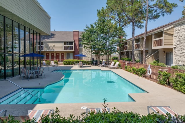 Outdoor community pool with deck chairs, umbrellas, and surrounding apartment buildings.