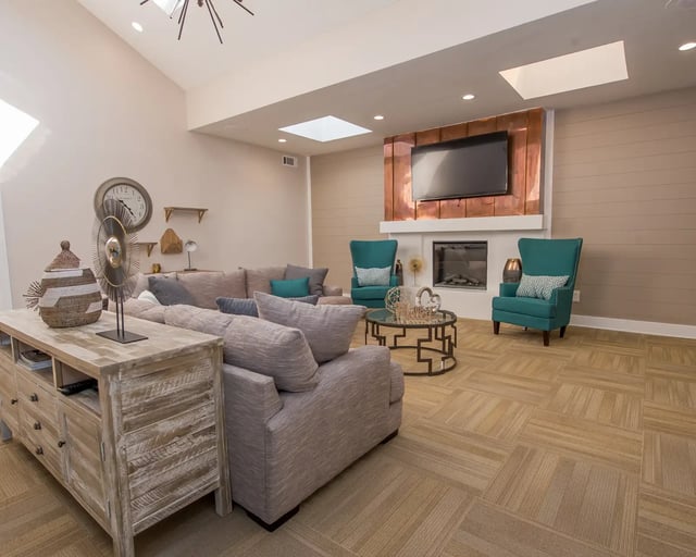 Spacious living room with a large sectional sofa, two teal accent chairs, a fireplace, and a TV mounted above the mantel.