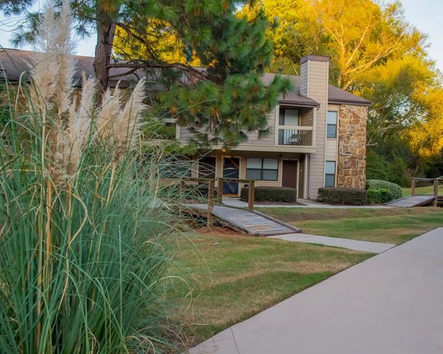 Exterior view of a multi-family building with a wooden ramp, walkway, and landscaped lawn.