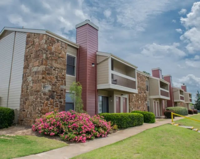 Exterior view of apartment buildings with stone accents, balconies, and landscaped grounds.