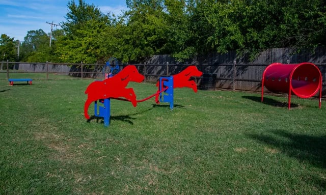 Outdoor community playground with red horse-jump structures and a red tunnel on a grassy field.