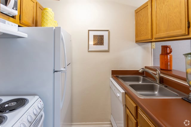 Kitchen with white refrigerator, electric stove, double sink, and wooden cabinets.