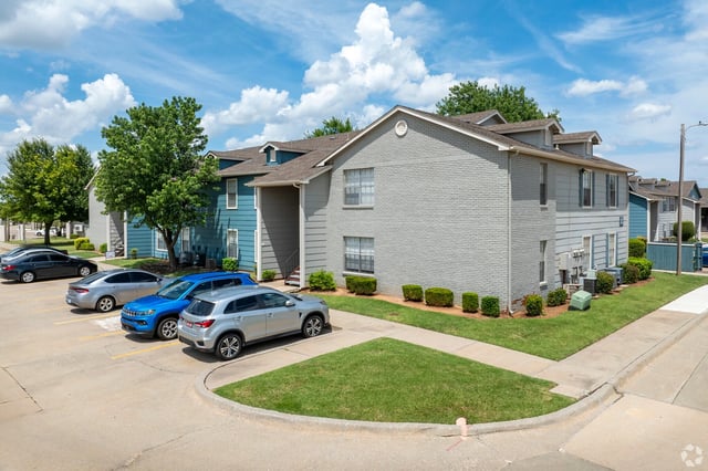 Exterior view of a multi-building apartment community with parked cars and landscaped grounds.
