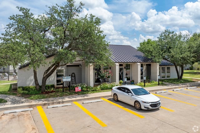 Exterior of a single-story leasing office with a metal roof, parking lot, and trees.