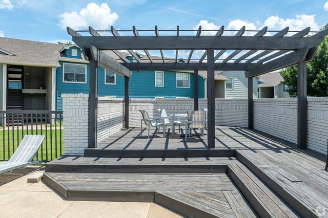 Outdoor communal deck with a dark wooden pergola, seating area, and white brick walls.