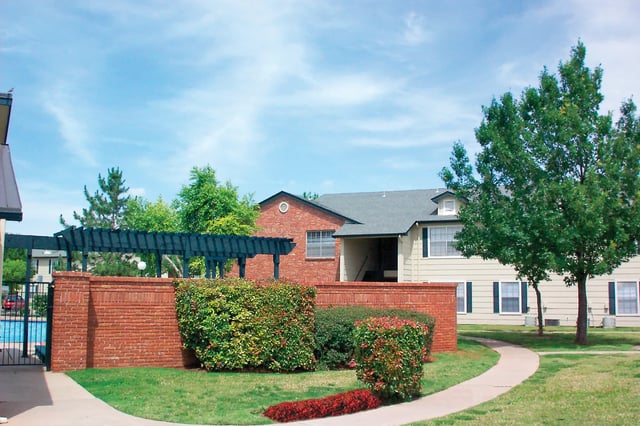 Exterior view of a brick apartment building with landscaping and a curved walkway.