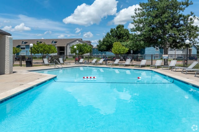 Outdoor pool area of an apartment community with lounge chairs and fencing.