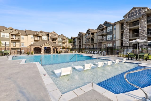 View of a swimming pool with lounge chairs and apartment buildings in the background