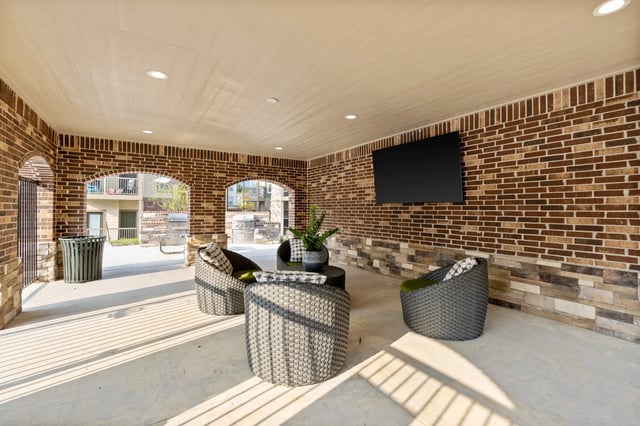 Covered outdoor seating area with brick walls and a TV.