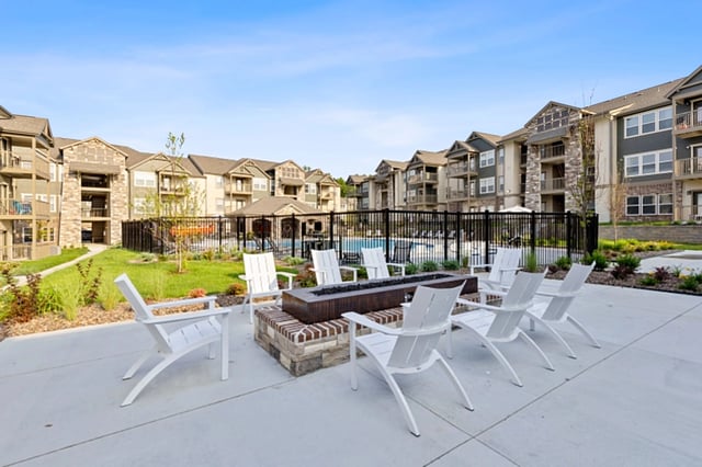 A patio with white chairs and a fire pit in front of apartment buildings.