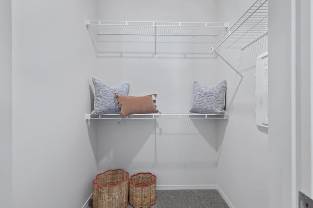 Closet with wire shelving, two wicker baskets, and decorative pillows.