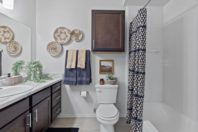Modern bathroom with dark wood vanity, marble countertop, decorative wall baskets, and a patterned shower curtain.