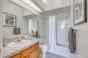 Modern bathroom with granite countertop vanity, toilet, and shower/tub combo with white curtain.