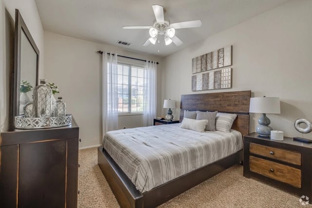 Queen bed with striped comforter and wooden headboard, nightstand, dresser, and ceiling fan.