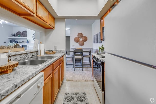 Kitchen with wood cabinets, granite countertops, double sink, dishwasher, and adjacent dining area.